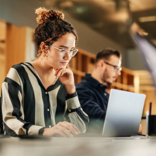 Portrait of Enthusiastic Hispanic Young Woman Working on Computer in a Modern Bright Office. Confident Human Resources Agent Smiling Happily While Collaborating Online with Colleagues.